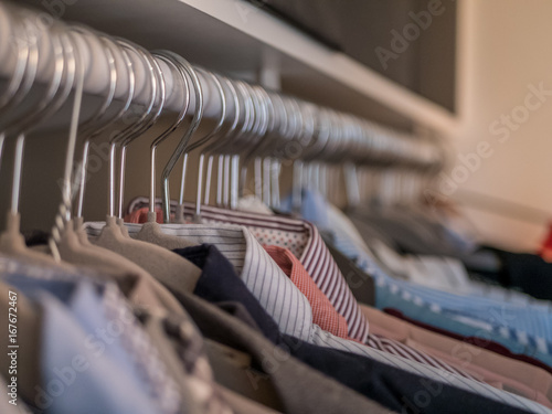 Men's shirts in different colors on hangers in wardrobe. © Adam