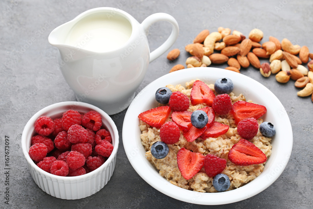 Oatmeal in plate with berries, nuts and jar of milk on wooden table Oatmeal in plate with berries, nuts and jar of milk on wooden table