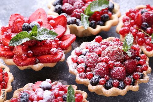 Dessert tartlets with berries and powdered sugar on grey wooden table