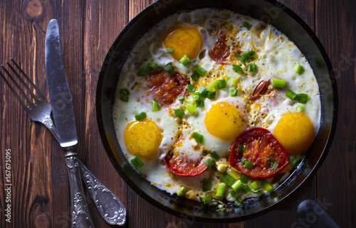 Eggs fried tomatoes in a cast-iron frying pan Wooden vintage background 