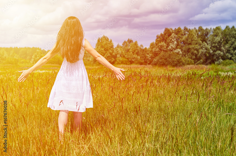 Φωτογραφία The girl in the dress is walking along the field with her arms outstretched