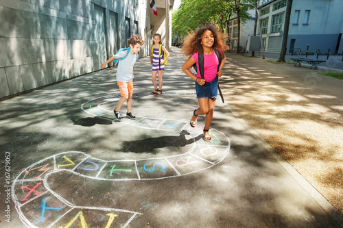 Three happy school age kids play hopscotch