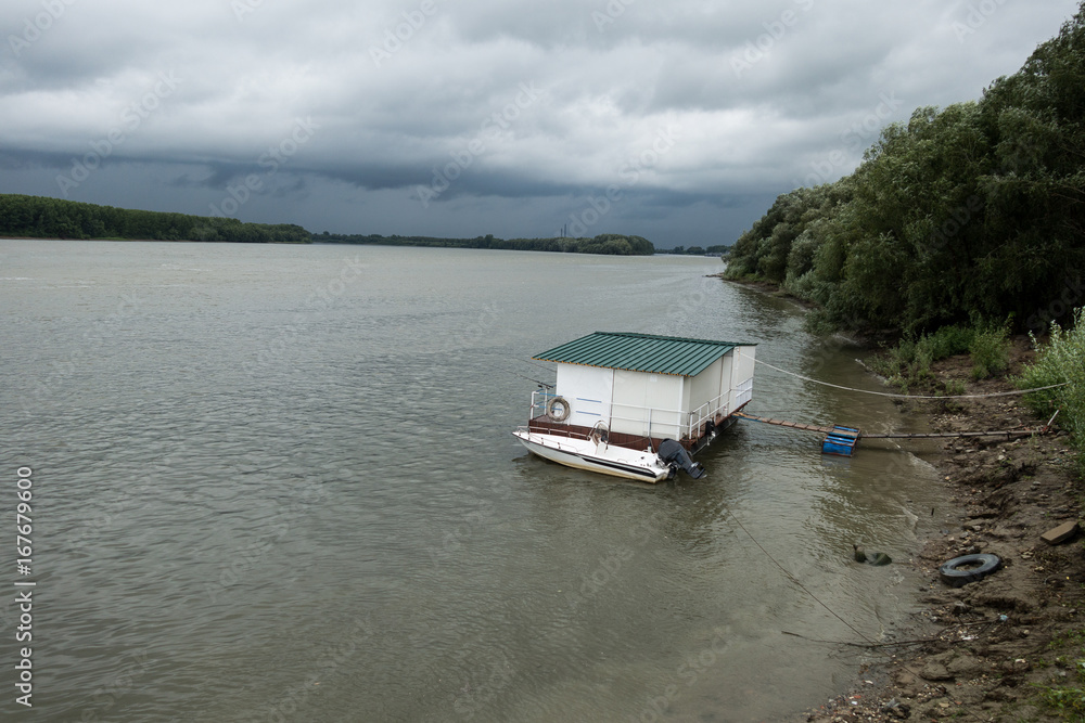Boat and pontoon alongside Danube river, in Braila, Romania, stormy spring day