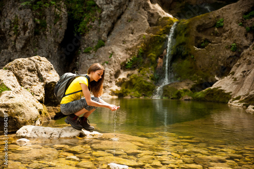 active young woman drinking water from a mountain creek on a warm spring day