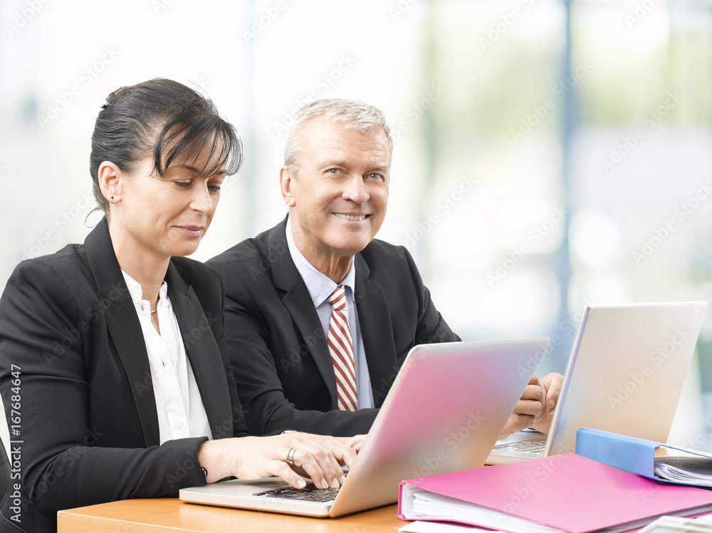 Business team at work. Shot of an senior investment advisor businessman and his female financial assistant analyzing financial data while working on laptops. Business team at work. Shot of an senior investment advisor businessman and his female financial assistant analyzing financial data while working on laptops.
