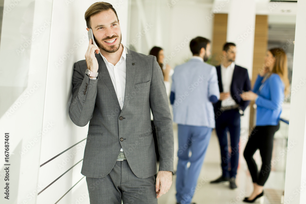 Businessman with mobile phone in office while other business people talking in background Businessman with mobile phone in office while other business people talking in background