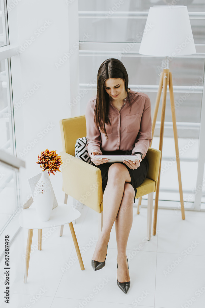 Young businesswoman sitting on a chair and holding tablet in hands Young businesswoman sitting on a chair and holding tablet in hands