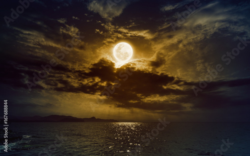 Rising yellow full moon in dark night sky with reflection in water