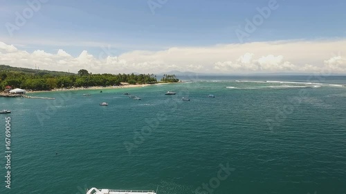 Aerial view of Senggigi beach with turquoise water, flying above boats towards palm trees in Lombok island shore. Shot with drone on sunny day with blue sky in Indonesia. photo