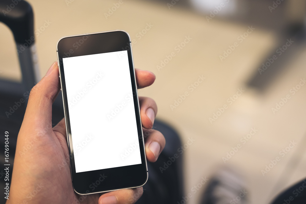 Mockup image of a man's hand holding and using black mobile phone with blank white screen with black baggage in airport