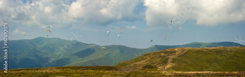 Competitions of paragliders on the ridge of Borzhava in the Carpathians in Ukraine. Panoramic photo of a large group of paragliders in the sky above the mountains.