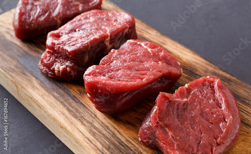 Raw beef filet mignon steaks on wooden board at gray background