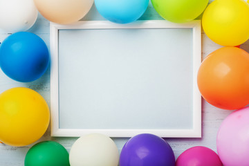 Colorful balloons and white frame on blue wooden table top view. Mockup for planning birthday or party. Flat lay style. Copy space for text. Festive greeting background.