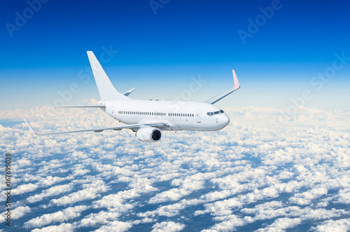 White airplane flies high in the sky above the clouds blue sky