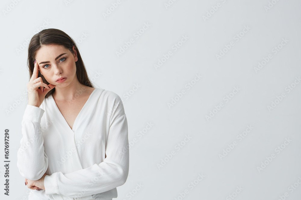 Displeased young beautiful businesswoman thinking looking at camera with finger near temple over white background. Displeased young beautiful businesswoman thinking looking at camera with finger near temple over white background.
