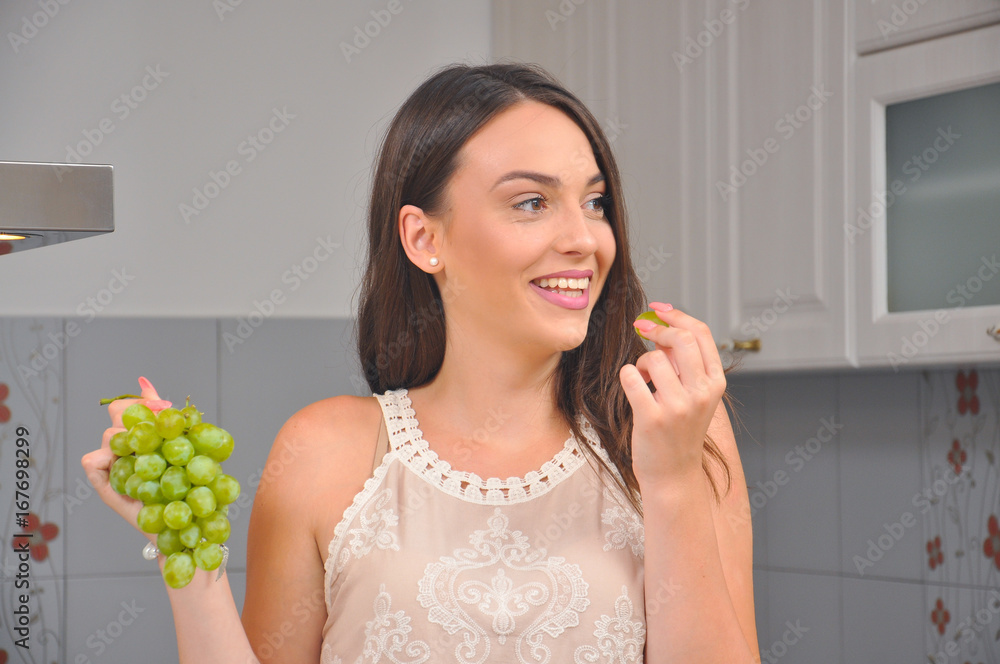 Beautiful smiling girl eats grapes in the kitchen. Teenage girl eating grapes for breakfast Beautiful smiling girl eats grapes in the kitchen. Teenage girl eating grapes for breakfast