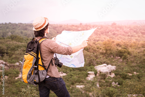 young tourist with a backpack standing on top of a hill holding a map and watching the sunset in beautiful sunset.