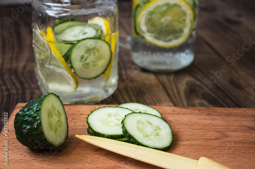 Cucumber and lemon slices on a cutting board and a jar on the background
