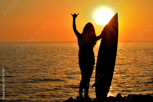 silhouette woman on coast holding surfboard at sunset