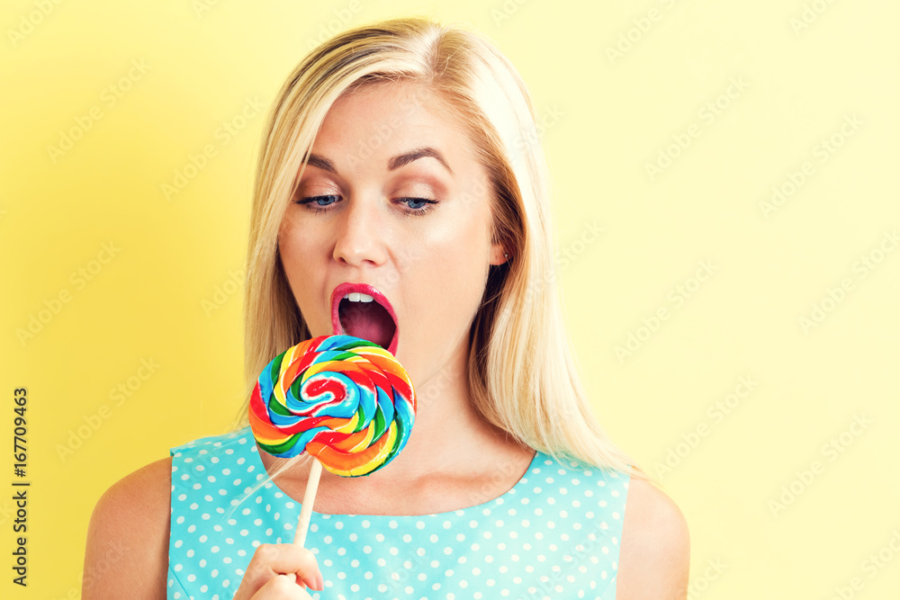 Young woman holding a lollipop on a yellow background