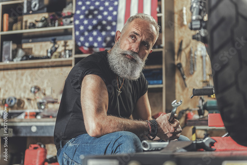 Thoughtful mature man holding tool in reapair shop photo