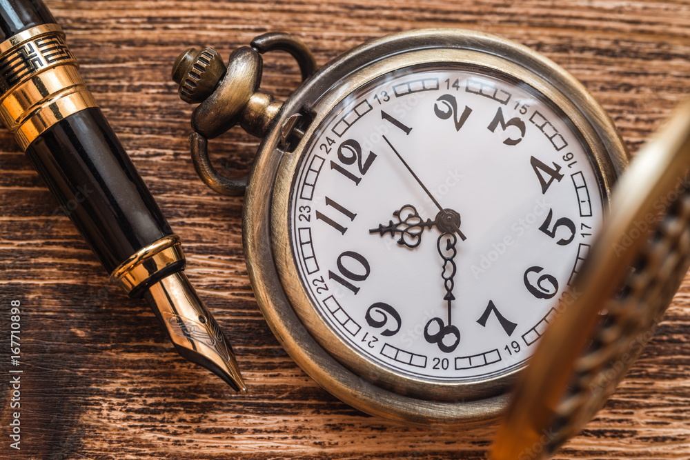 Pocket watch and pen on a wooden background