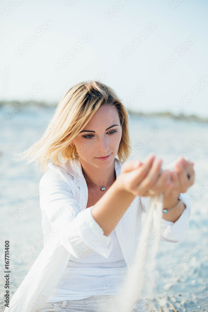 Girl sitting on sand at the beach. In her open palms sand that pours through her fingers.