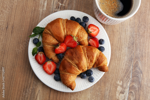 Delicious breakfast with fresh croissants, coffee and ripe berries on old wooden background