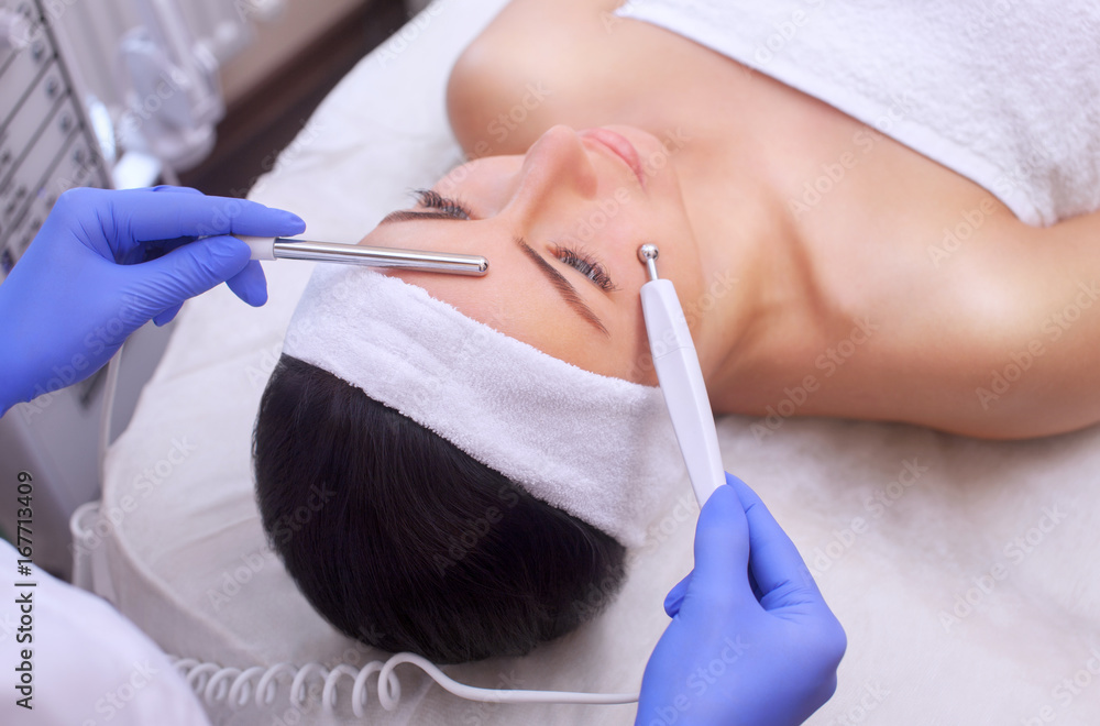 The physician-cosmetologist makes Electric Facial Treatment of the skin of a beautiful, young woman in a beauty salon. Cosmetology and professional skin care. The physician-cosmetologist makes Electric Facial Treatment of the skin of a beautiful, young woman in a beauty salon. Cosmetology and professional skin care.