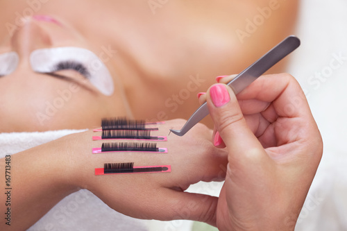 The procedure for eyelash extensions in the beauty salon, eyelashes on the hand of the make-up artist. In the background a girl with long eyelashes.