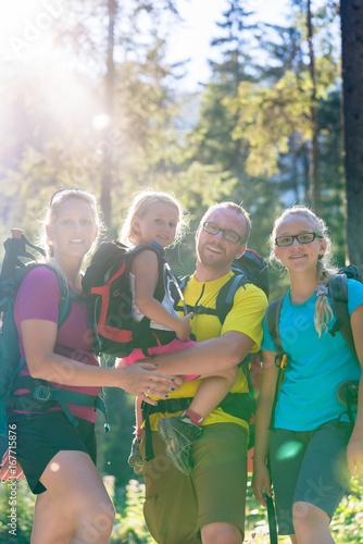 Family with two daughters on hike in the woods backlit in summer © Kzenon