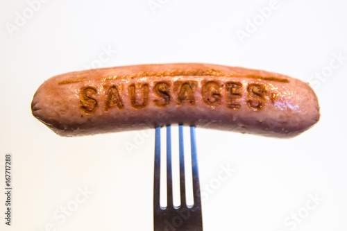 Fotografia sausage with an inscription pinned on a fork, on a white background