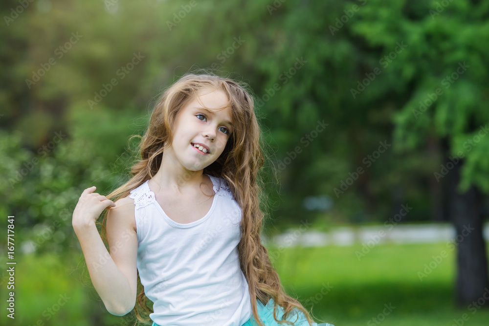 Portrait of beautiful smiling Caucasian little girl with long curly hair against the background of a green park Happy childhood concept Portrait of beautiful smiling Caucasian little girl with long curly hair against the background of a green park Happy childhood concept