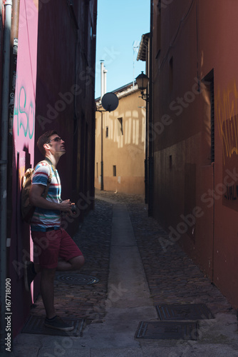 Retrato diurno de hombre con cámara de fotos en callejón oscuro desierto iluminado parcialmente.