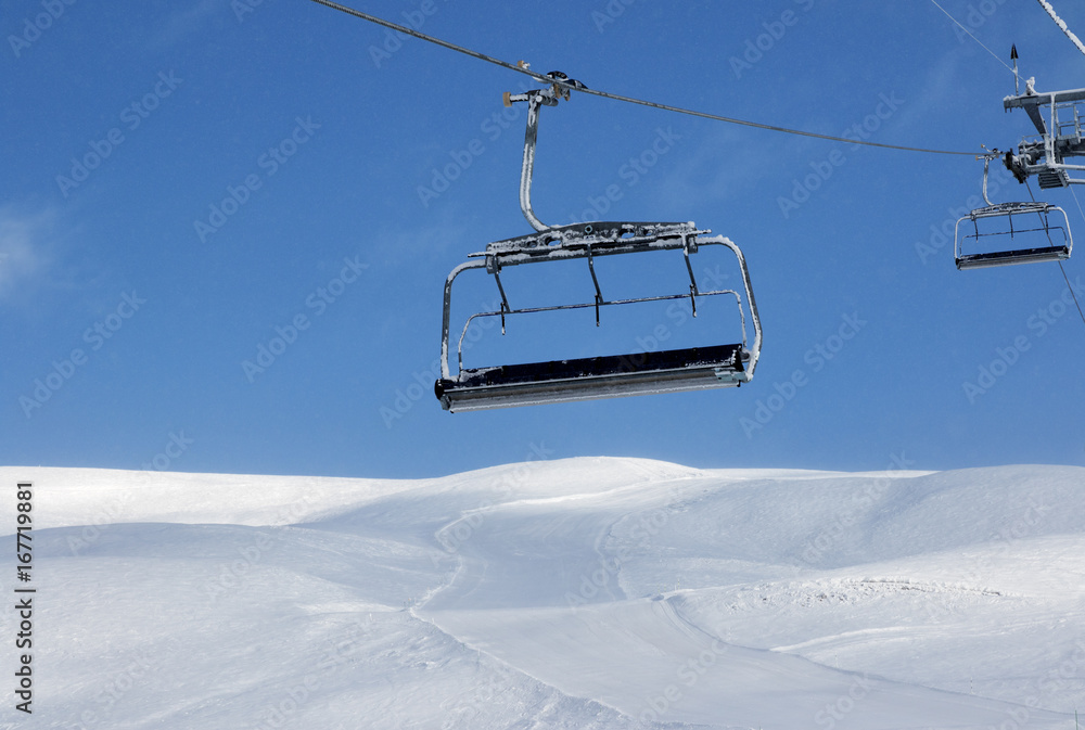 Ski slope, chair-lift on ski resort and blue sky with falling snow