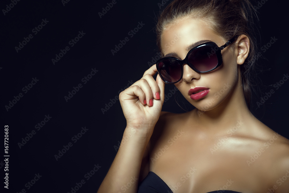 Close up portrait of young gorgeous glam tanned model with casual updo hair and beautiful make up wearing trendy classic sunglasses. Isolated on black background. Copy-space. Studio shot Close up portrait of young gorgeous glam tanned model with casual updo hair and beautiful make up wearing trendy classic sunglasses. Isolated on black background. Copy-space. Studio shot