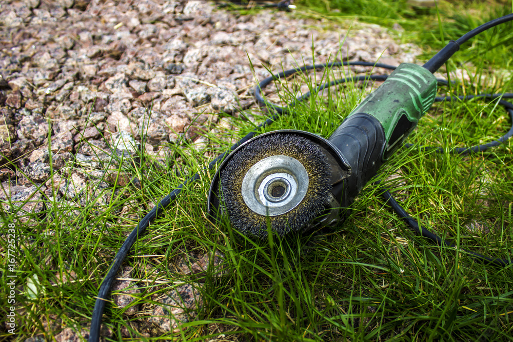 Naklejka premium Hand power tool - grinder with a nozzle attachment, top view, on grass and stones, outdoors