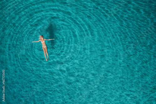Aerial view of swimming woman in Blue Lagoon. Mediterranean sea in Oludeniz, Turkey. Summer seascape with girl, clear azure water, waves at sunrise. Transparent water.Top view from flying drone.Travel