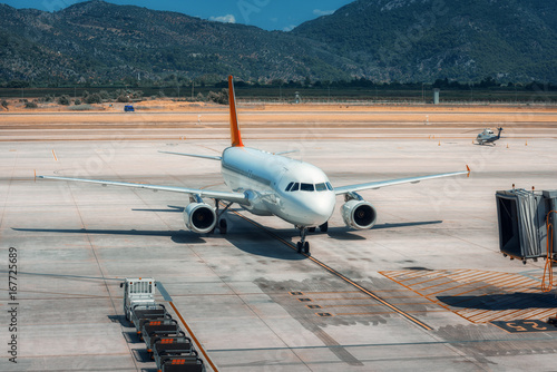 Beautiful white airplane on the runway in Dalaman airport. Landscape with big passenger airplane is taking off and mountains at bright sunny day in summer. Business trip. Commercial aircraft. Travel photo