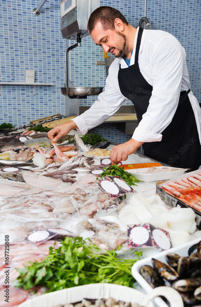 Seller in black apron shows fish counter
