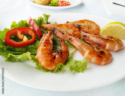 Grilled tiger shrimps served on white plate with lettuce and lemon. Seafood. Mediterranean cuisine