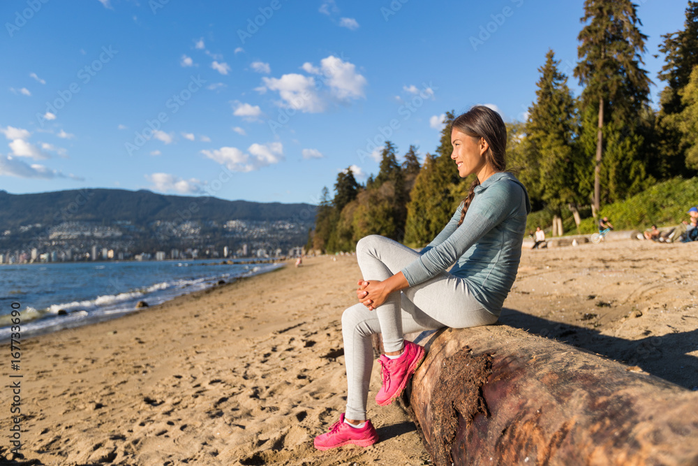 Fototapeta premium Kobieta miejskiego stylu życia Vancouver relaksująca się na Third Beach w Stanley Park, Vancouver, BC, Kanada. Kanadyjska dziewczyna azjatyckich siedzi na pniu drzewa w popularnej piaszczystej części wypoczynkowej kanadyjskiego miasta.