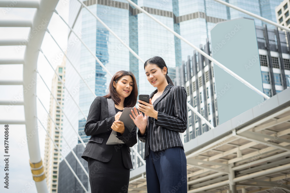 Two business woman standing using smartphone and discussing in front of the office. Business working concept. Two business woman standing using smartphone and discussing in front of the office. Business working concept.