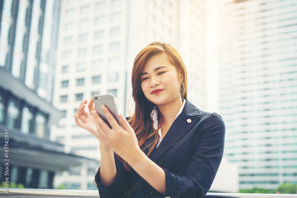 Young asian businesswoman using at mobile smartphone.Young female professional in the city in front of big building. Young asian businesswoman using at mobile smartphone.Young female professional in the city in front of big building.
