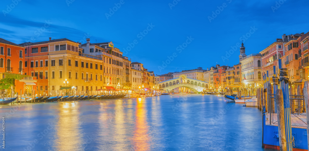 Rialto Bridge (Ponte di Rialto) or Bridge of Sighs and view of the most beautiful canal of Venice - Grand Canal and boats, gondolas, mansions along. Night view. Italy.