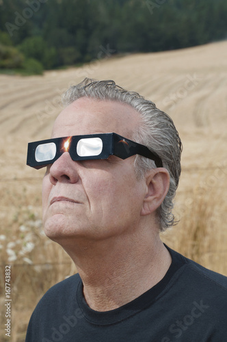 Man looking at the solar eclipse with eclipse glasses/Man viewing solar eclipse with solar glasses in country field/