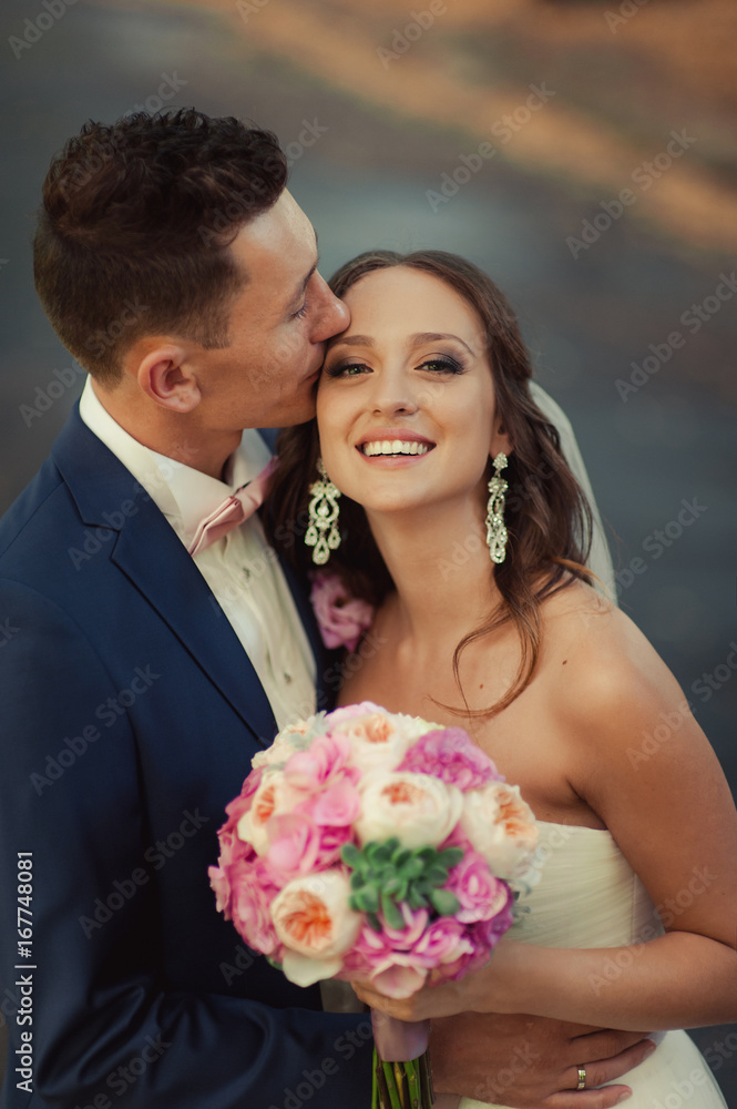 Beautiful bride and groom embracing and kissing on their wedding day Beautiful bride and groom embracing and kissing on their wedding day