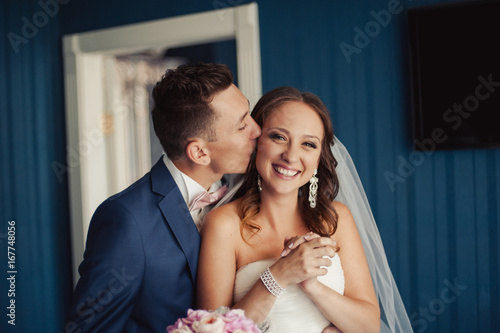 Tela Beautiful bride and groom embracing and kissing on their wedding day