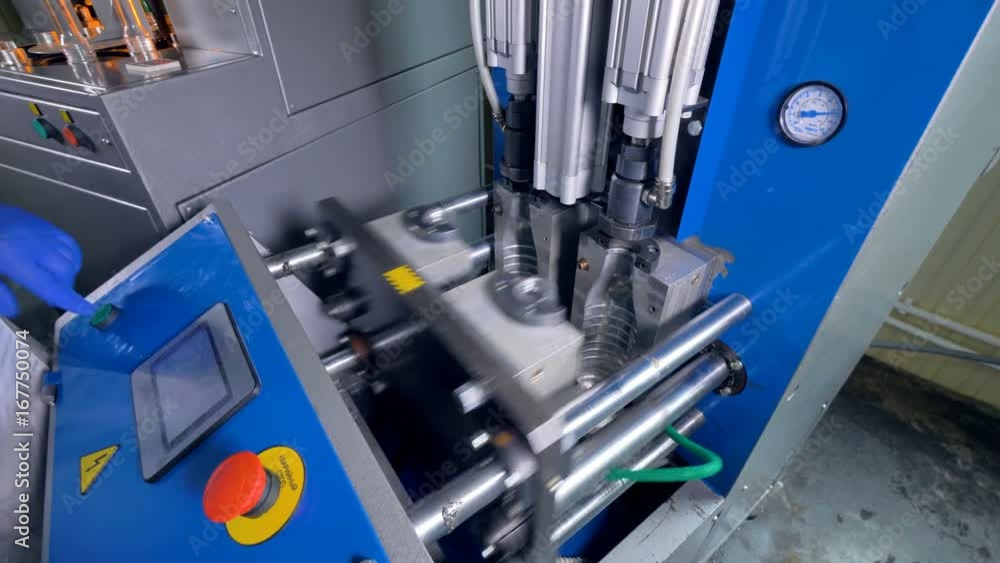 A worker installs preforms into a ridged blow-molding machine. A worker installs preforms into a ridged blow-molding machine.