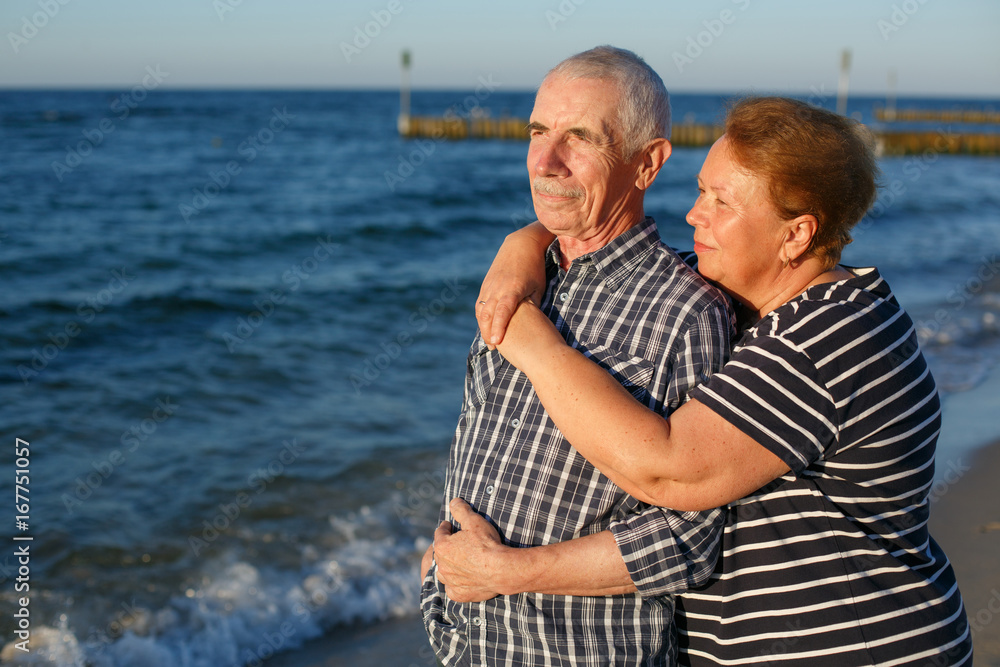 Happy family of two mature people hugging outdoors. Senior smiling couple standing on beach near sea on sunset. Happy family of two mature people hugging outdoors. Senior smiling couple standing on beach near sea on sunset.